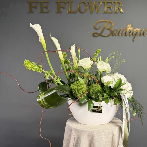 Modern white and green floral arrangement with calla lilies and roses in a low white ceramic bowl