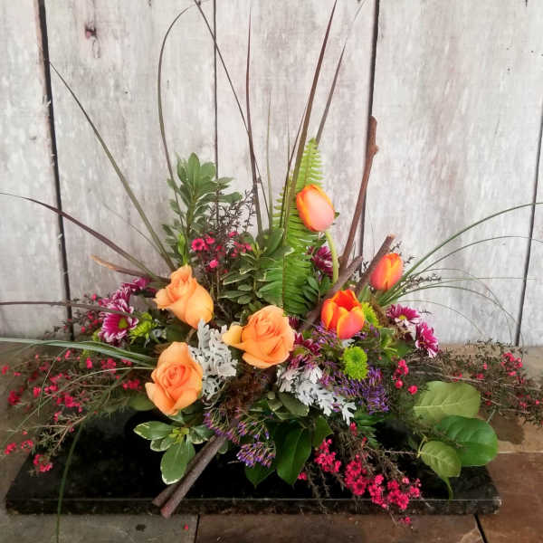 Low floral arrangement with orange roses and tulips in a black container