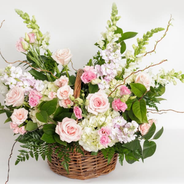 Pastel pink and white flower basket with roses, snapdragons, and other blooms in a woven wicker basket