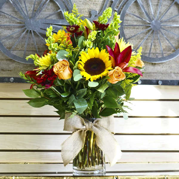 Bouquet of sunflowers, roses, and lilies in a glass vase with a burlap bow