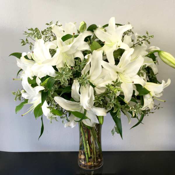 Tall clear vase of white lilies with variegated foliage