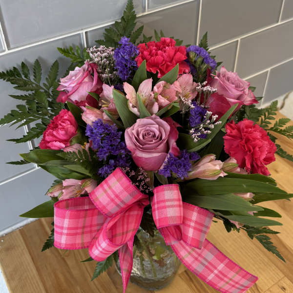 Bouquet of pink and purple flowers in a glass vase with a pink plaid ribbon