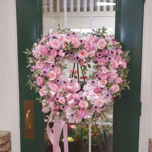 Heart-shaped pink floral wreath on a stand with ribbon