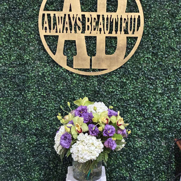 Purple and white floral arrangement in a glass vase beneath a gold monogram sign