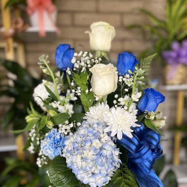 Blue and white flower bouquet in a glass vase with a blue ribbon