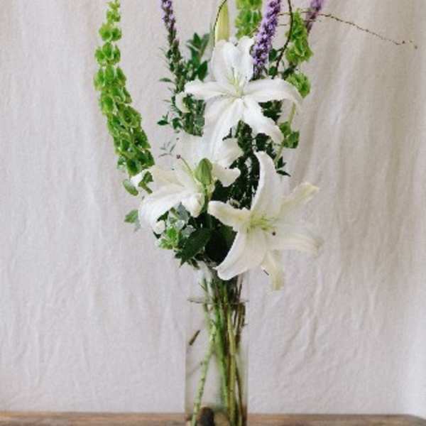 Tall white lily arrangement with green and purple spikes in a glass vase