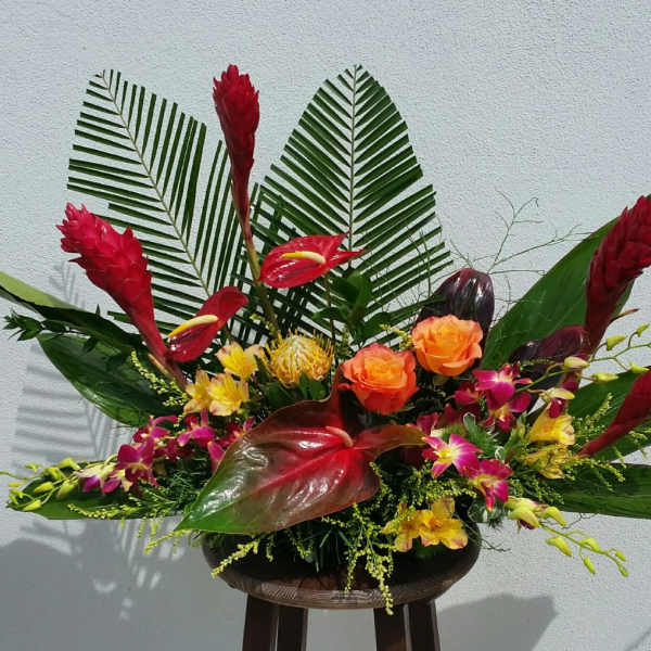 Tropical flower arrangement with red and orange blooms in a low container