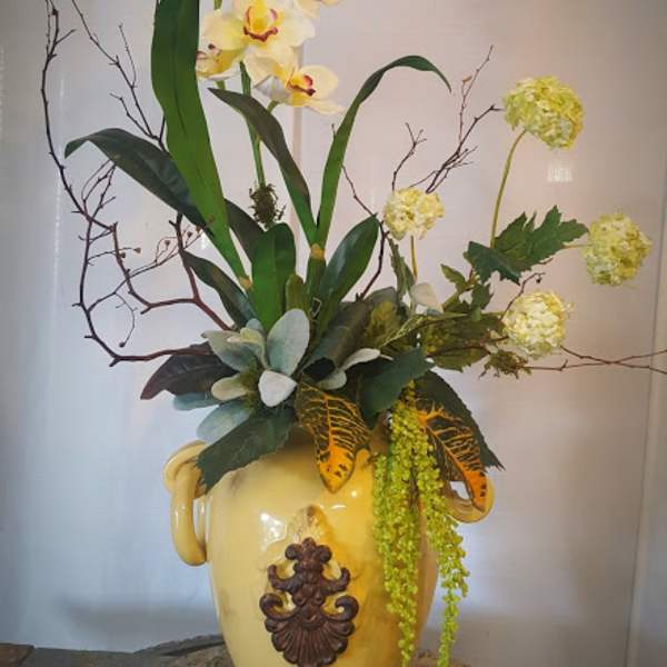 Tall floral arrangement with yellow orchids in a decorative ceramic vase