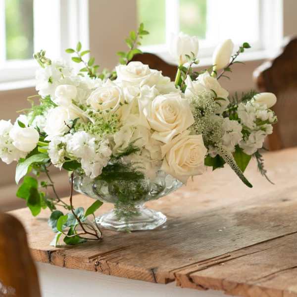 White roses and white blooms arranged in a clear glass compote vase