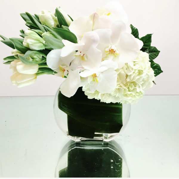 White orchids and pale tulips arranged in a clear glass vase