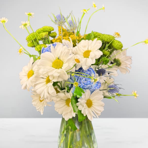 White daisies and blue flowers in a clear glass vase