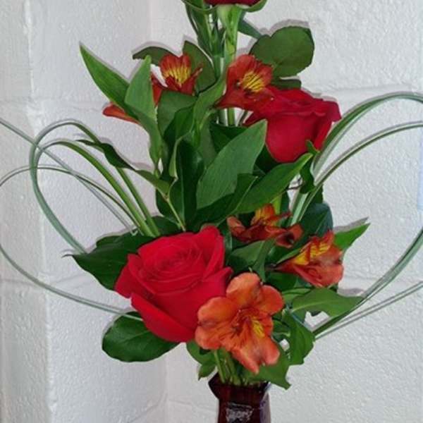 Red roses and orange alstroemeria in a tall vase arrangement