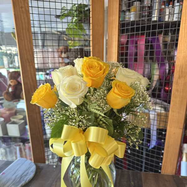 Yellow and white roses in a glass vase with a yellow ribbon