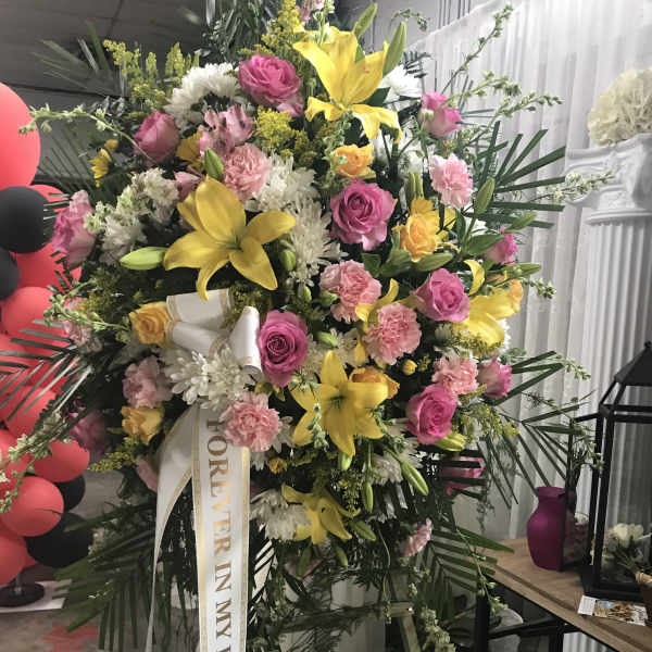 Large standing floral spray with pink and yellow flowers and a memorial ribbon
