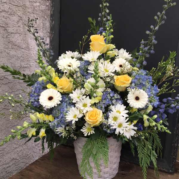 Basket arrangement of yellow roses, white daisies, and blue flowers