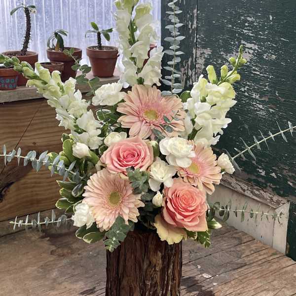 Pink roses and gerbera daisies in a rustic wood vase with white snapdragons