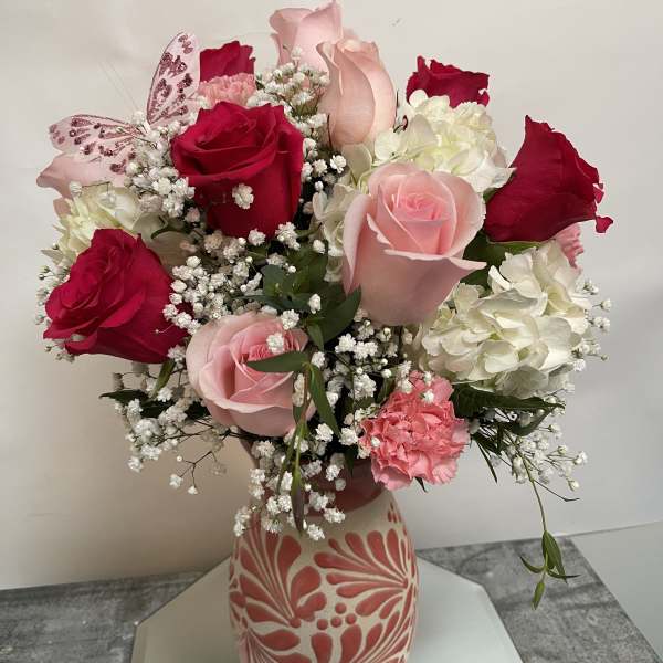 Bouquet of red and pink roses with white hydrangeas in a patterned vase