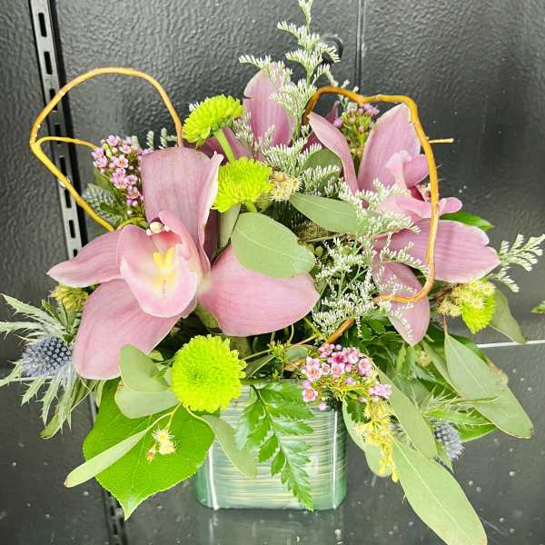 Compact arrangement of pink lilies and green button mums in a green glass cube vase