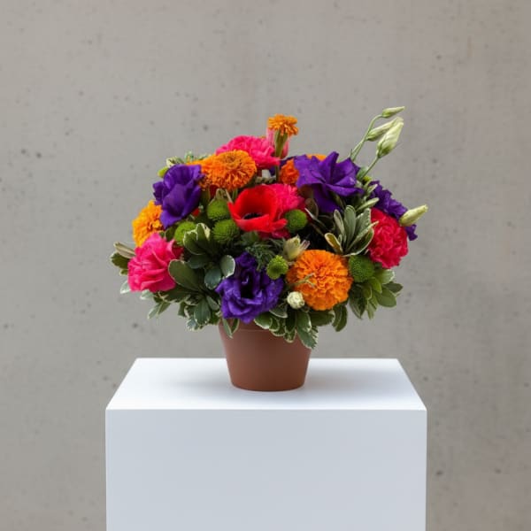 Bright mixed arrangement of orange, pink, purple, and red flowers in a small brown pot