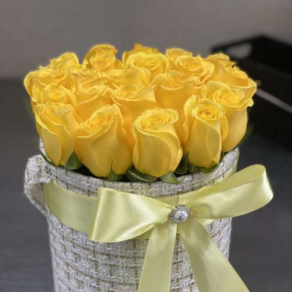 Yellow roses arranged in a round hatbox with a satin ribbon