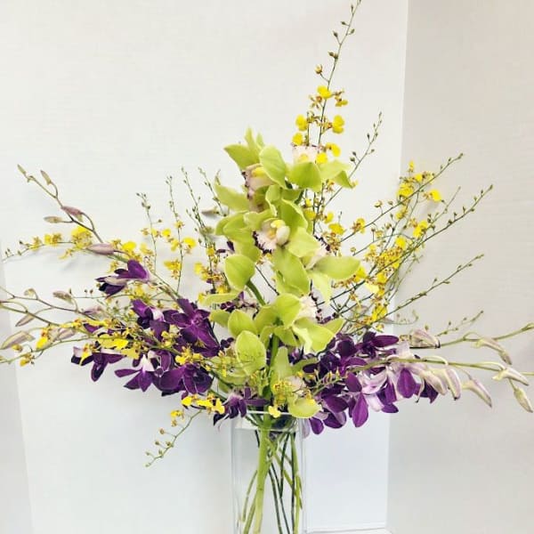 Tall orchid arrangement in a clear glass vase with yellow and purple blooms