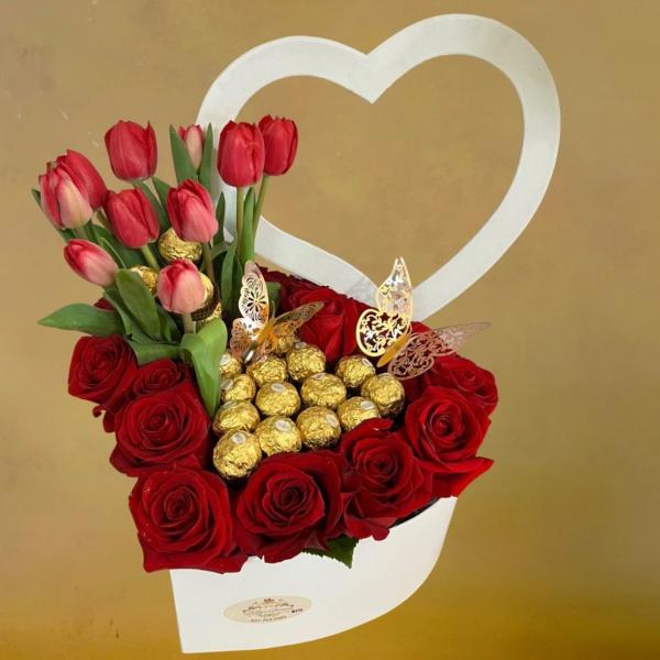 Heart-shaped white box with red roses, red tulips, and gold-wrapped chocolates.