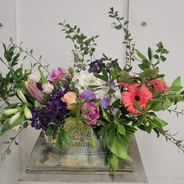 Mixed floral arrangement with roses, lilies, and gerbera daisies in a metal container