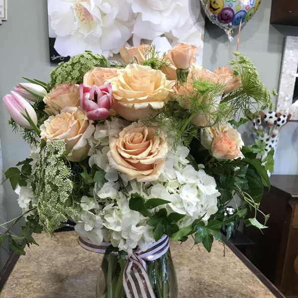 Peach roses and white hydrangeas in a glass vase with ribbon