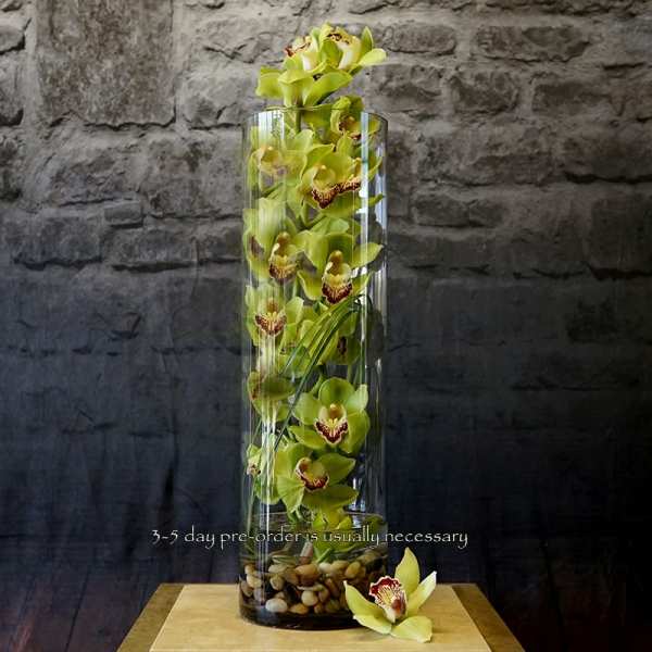 Tall glass vase filled with green orchids and pebbles