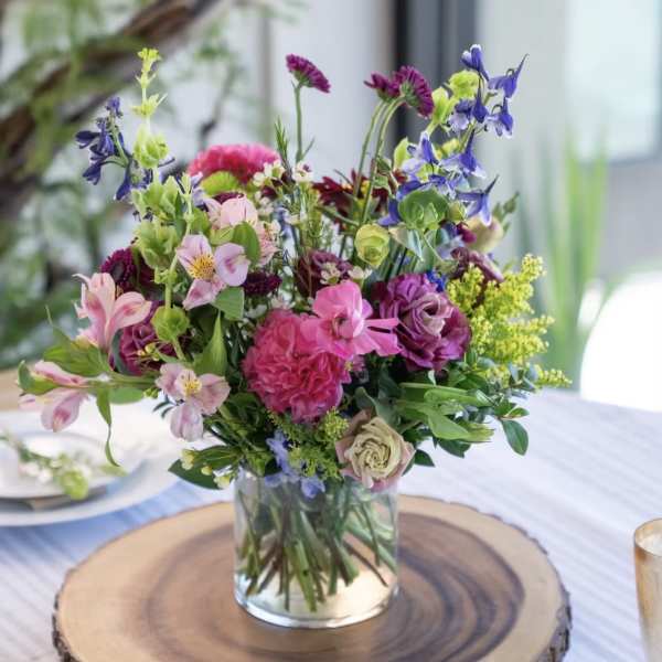 Mixed bouquet of pink, purple, and blue flowers in a clear glass vase