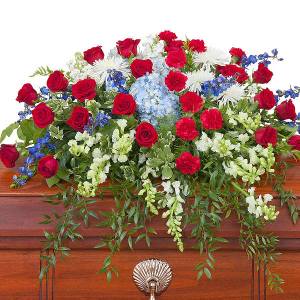 Red, white, and blue casket spray with roses, carnations, and mixed flowers on a wooden casket