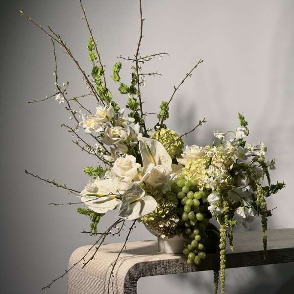 White floral arrangement with orchids, roses, and green grapes in a vase