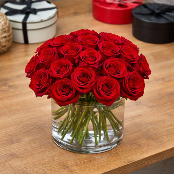 Low arrangement of red roses in a clear glass vase on a wooden table