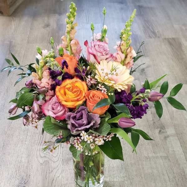Mixed bouquet of roses, snapdragons, and purple blooms in a glass vase