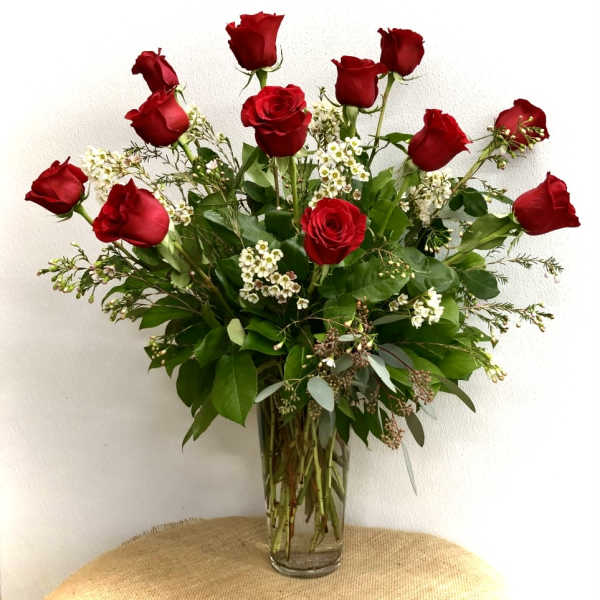 Red roses arranged in a clear glass vase with white filler flowers
