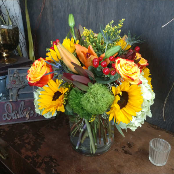 Mixed bouquet in a clear glass vase with sunflowers, roses, and lilies