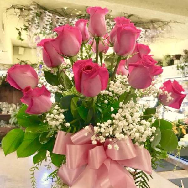 Pink roses arranged in a clear glass vase with a pink ribbon bow
