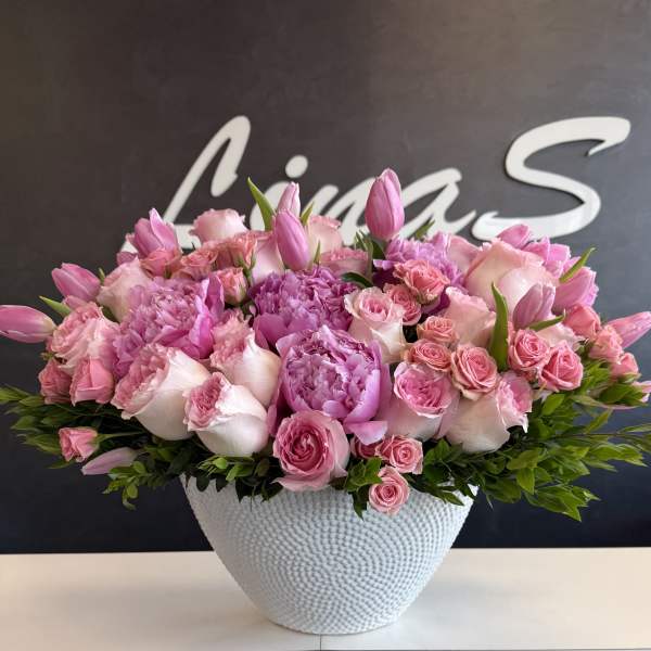 Low white bowl filled with dense pink peonies, roses, spray roses, and tulips