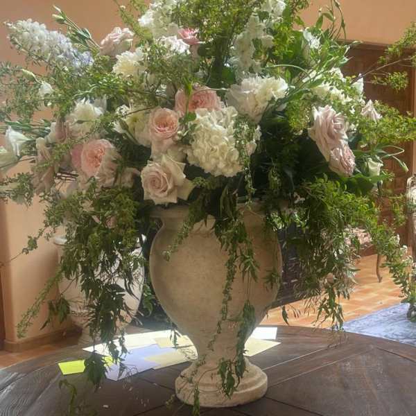 Large urn arrangement with white and blush flowers and cascading greenery on a round wooden table