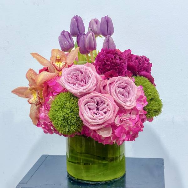 Pink and purple floral arrangement in a green glass vase