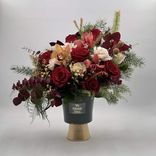 Red roses and pink orchids in a black vase with gold base