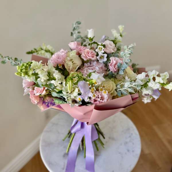 Pastel bouquet of pink, white, and lavender flowers wrapped in pink paper