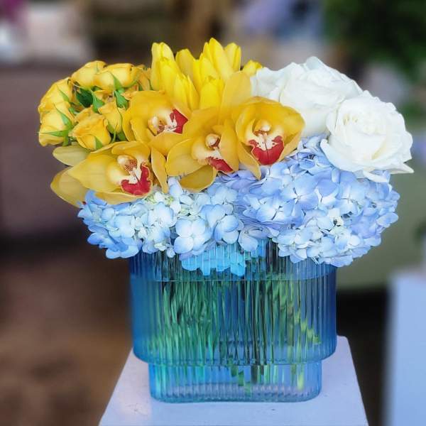 Yellow orchids, blue hydrangeas, and white roses in a blue glass vase