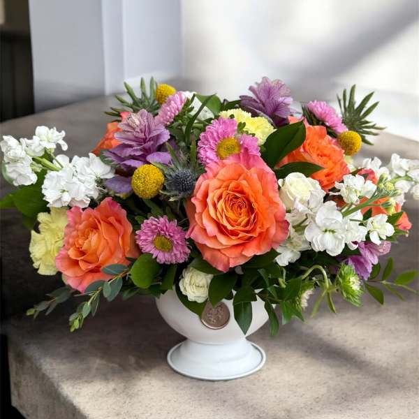 Colorful mixed flower arrangement in a white pedestal vase