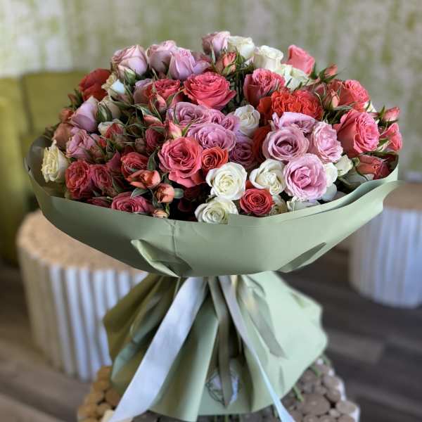 Large bouquet of pink, red, and white roses wrapped in pale green paper