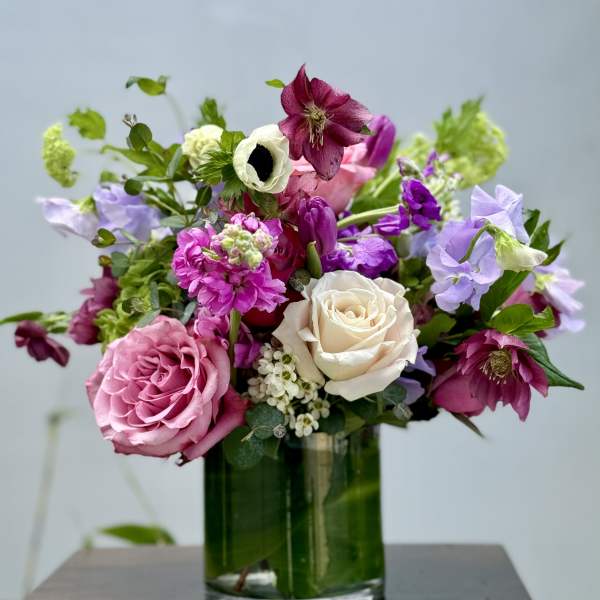 Pink and white roses with purple blooms in a glass vase