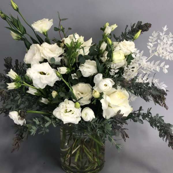 White floral arrangement in a glass vase with dark foliage