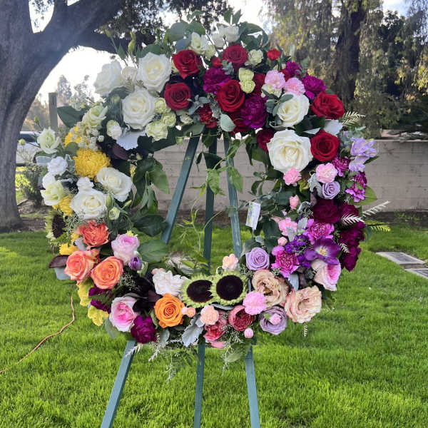 Large floral wreath on an easel with roses in red, white, pink, and purple