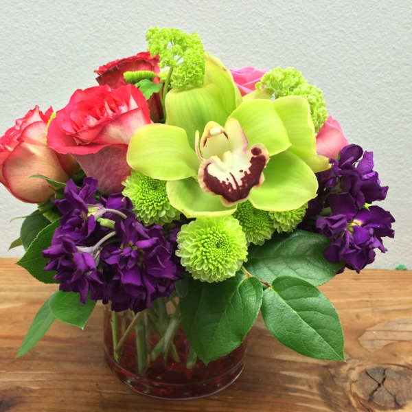 Bouquet of pink roses, green orchids, and purple flowers in a glass vase