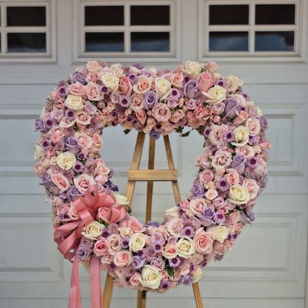 Heart-shaped floral wreath of pink, lavender, and cream roses on an easel